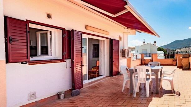 Eine Terrasse mit Tisch und Stühlen, einer Schiebetür und einem roten Sonnensegel.