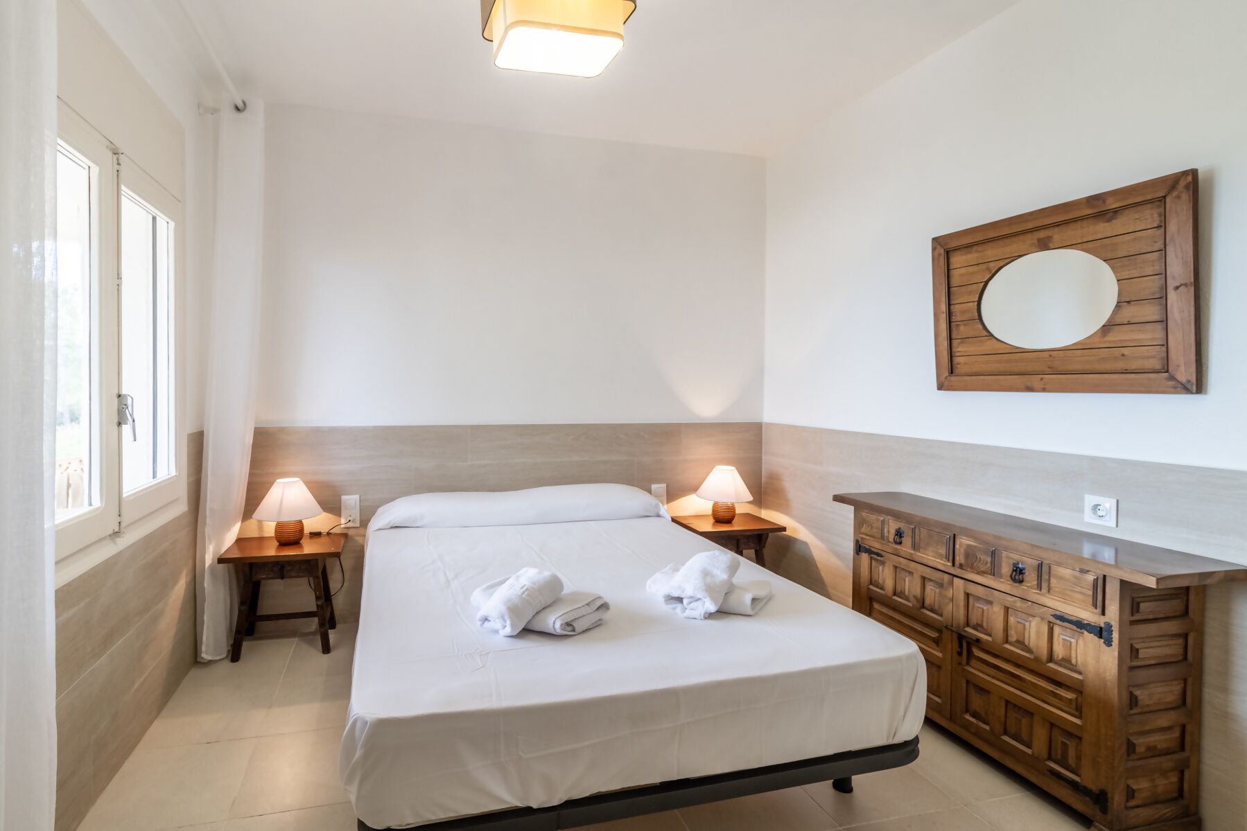 A hotel room with a bed, two bedside lamps, a wooden dresser, and a mirror on the wall.