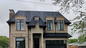 A two-story house with a stone facade, a black roof, and a garage. - Brand New Basement Apt next to Beach & Go Train (Pickering)
