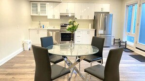 A modern kitchen with white cabinets, stainless steel appliances, and a glass dining table with four chairs. - Brand New Basement Apt next to Beach & Go Train (Pickering)