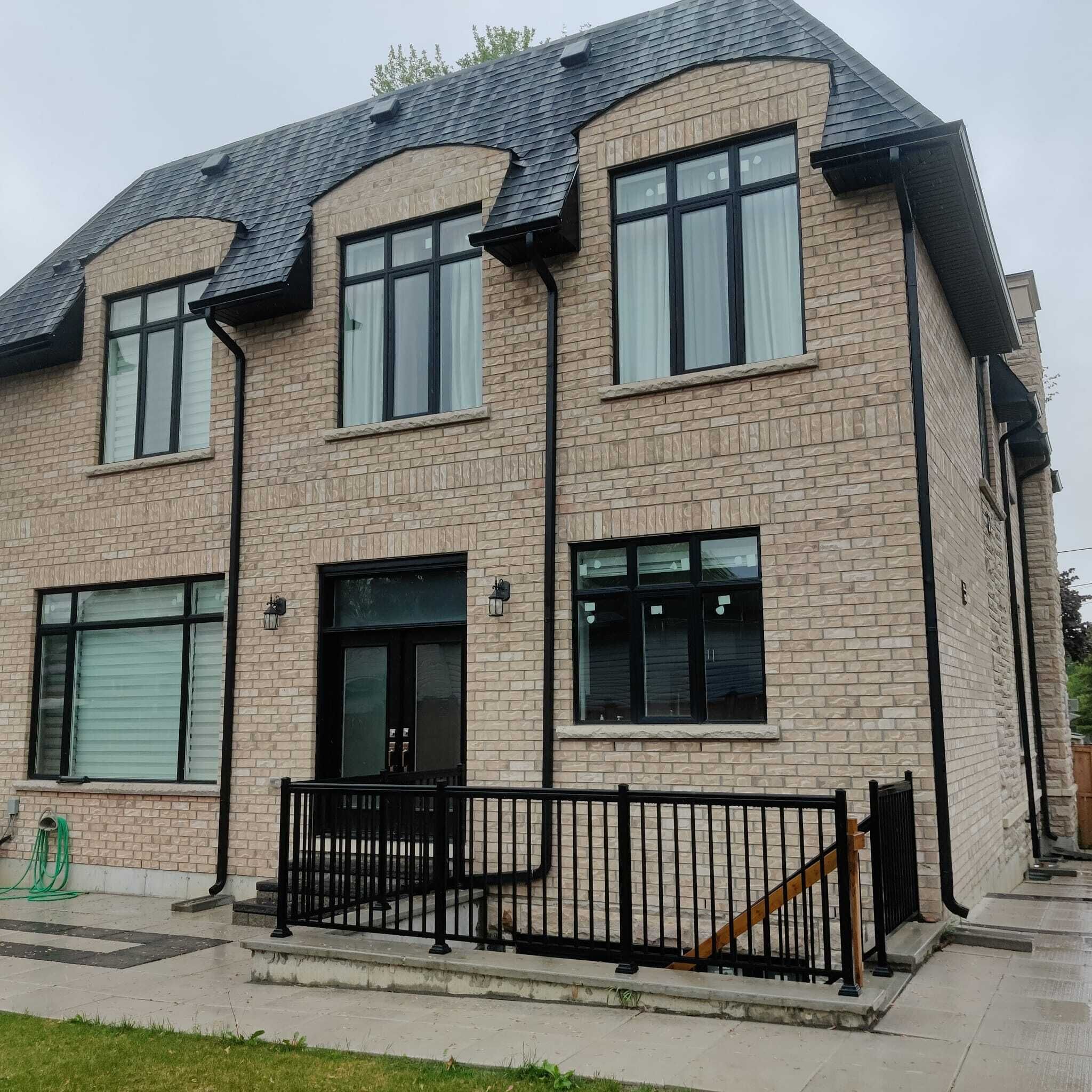 A two-story building with a brick facade, large windows, and a black metal fence in front.