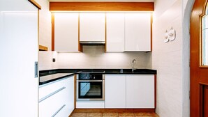 Una cocina compacta con armarios blancos, encimera negra y suelo de baldosas.