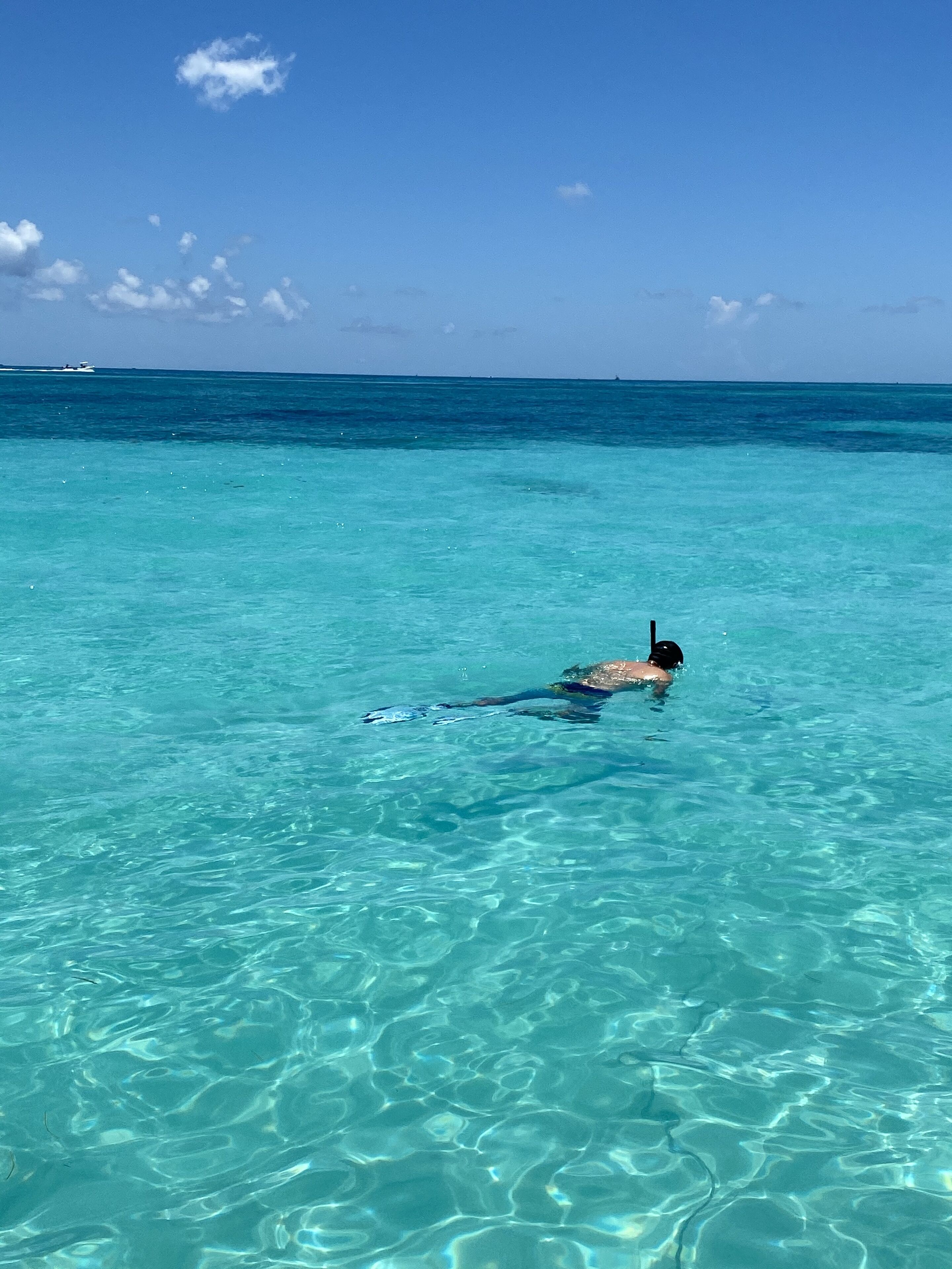 Iemand snorkelt in helder turquoise water, met een boot in de verte.