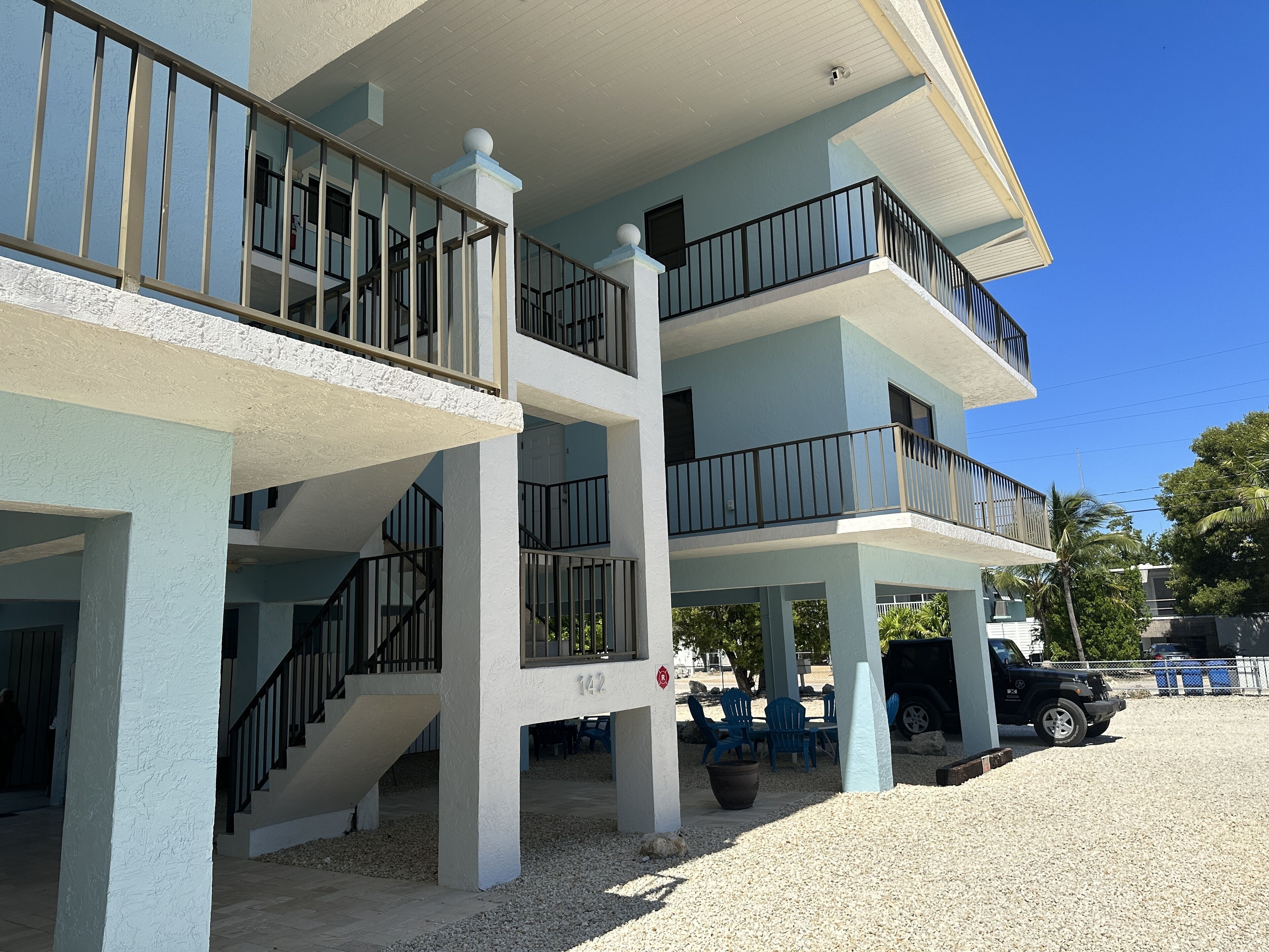 A multi-story building with balconies, outdoor seating, and a gravel driveway.