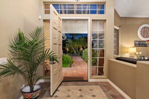 Um corredor com uma porta que dá para um jardim, uma planta em vaso e um relógio na parede.
