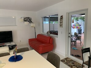 A living room with a red sofa, a white TV stand, and a dining table with chairs.