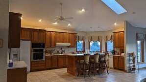 A spacious kitchen with wooden cabinets, a central island with bar stools, a ceiling fan, and a skylight.