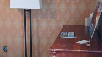A room with a wooden floor, a desk with a lamp, and a patterned wall.