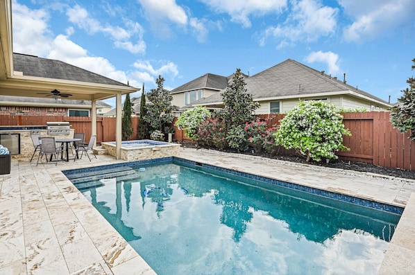 A backyard with a swimming pool, patio furniture, and a barbecue area.