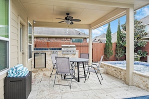 A covered patio with a grill, seating, and a view of a backyard.