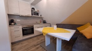 Cocina compacta con microondas, horno y cafetera. Una mesa blanca con mantel amarillo está en el centro.