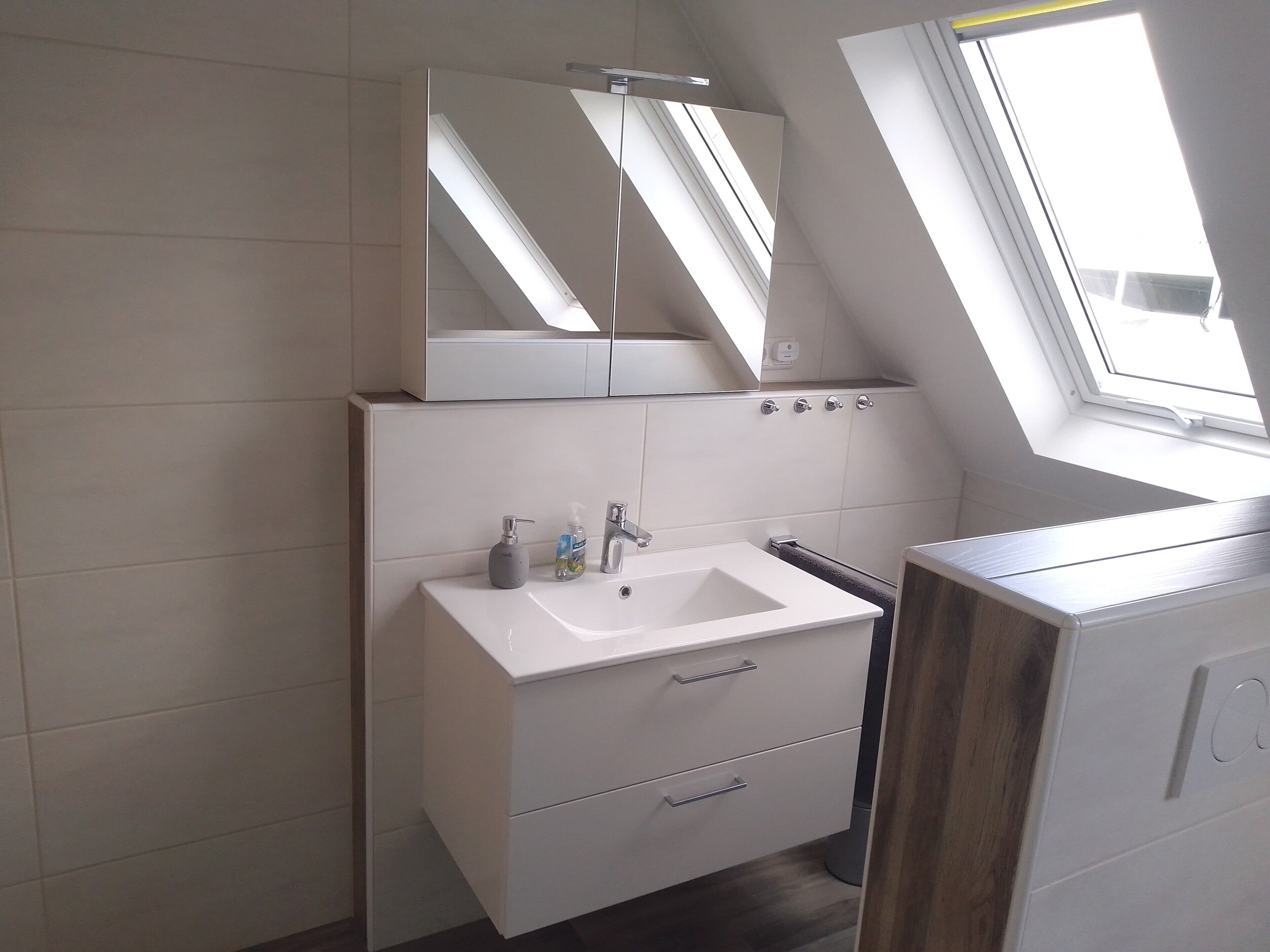 Une salle de bain moderne avec un puits de lumière, un lavabo blanc et un miroir au-dessus.