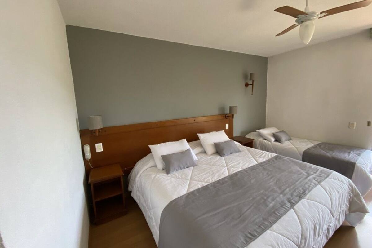 A bedroom with two beds, a ceiling fan, bedside lamps, and a nightstand.