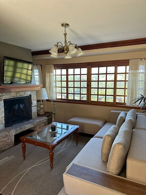 A living room with a stone fireplace, a flat-screen TV, a sofa, and a large window with curtains. - Constellation Lodge (Campos do Jordão)