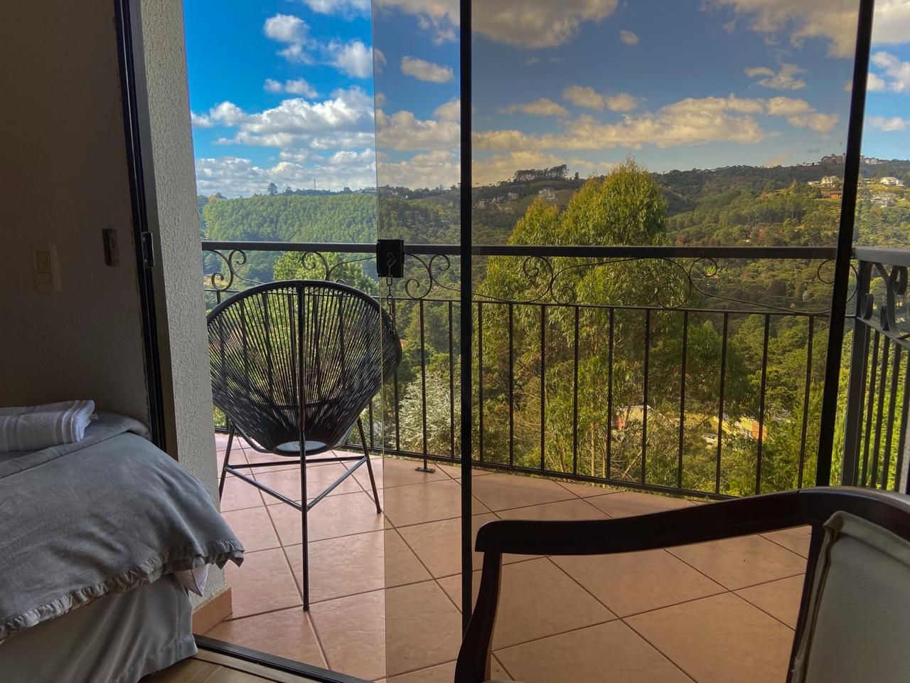 Uma varanda com vista para uma paisagem montanhosa, uma cadeira e uma cama.