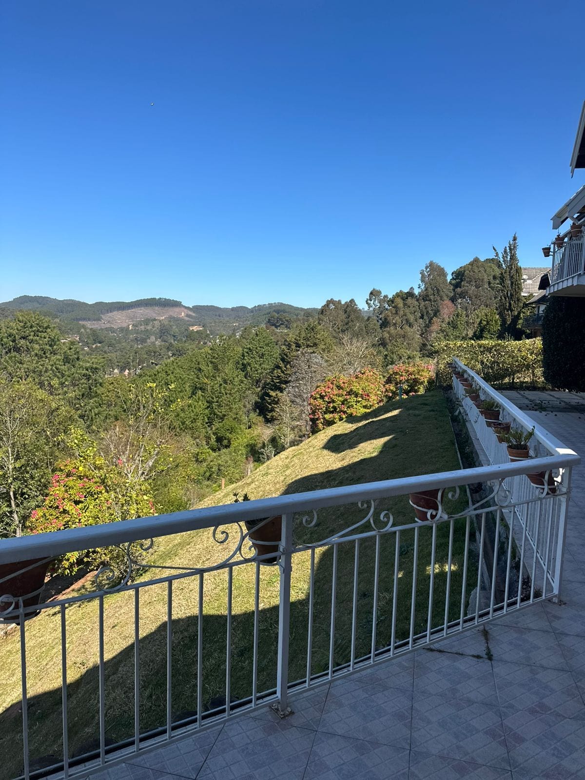 Varanda com grade de metal, vista para um jardim bem cuidado e colinas ao longe.