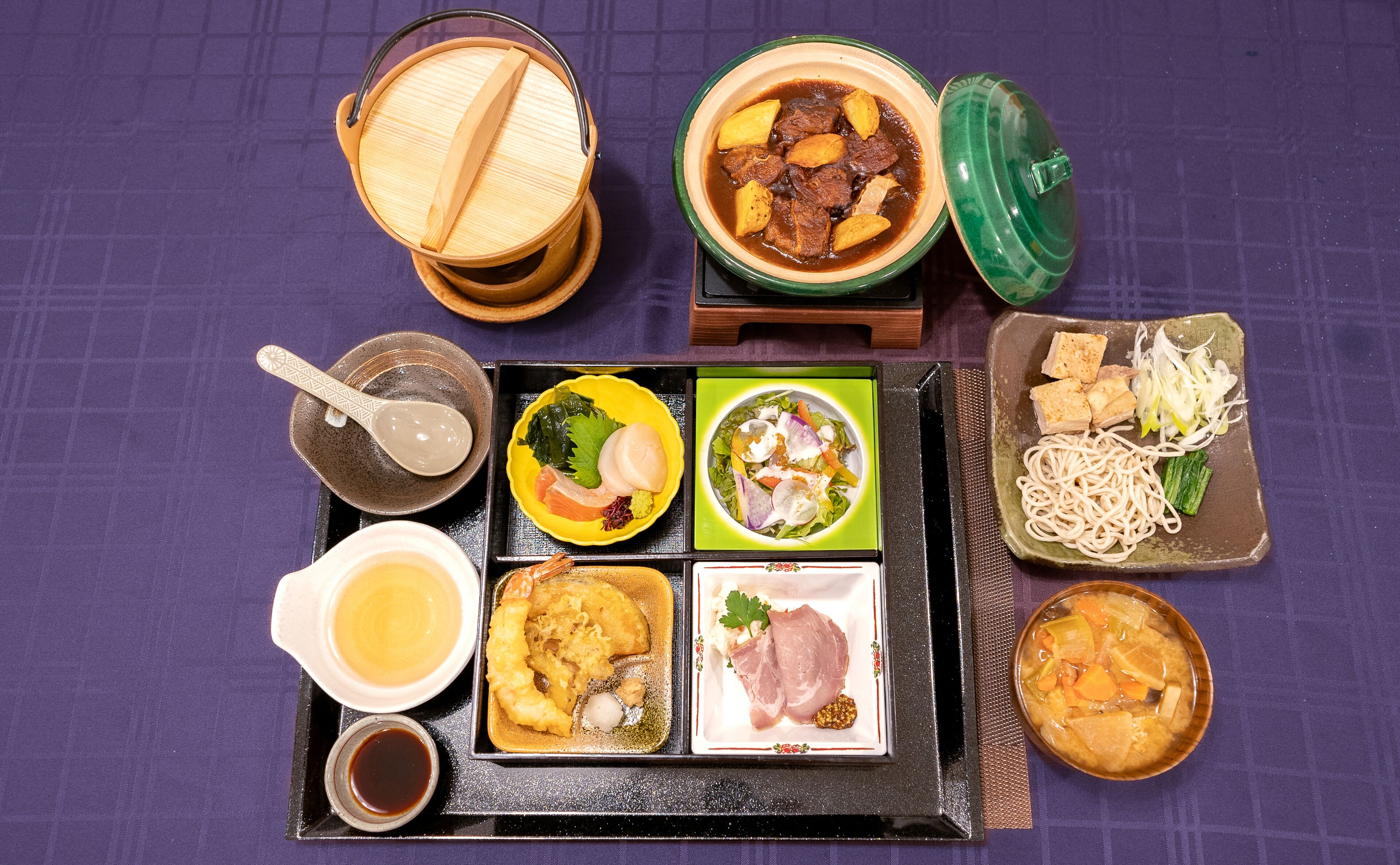 A variety of Japanese dishes arranged on a tray, including sushi, sashimi, and a bowl of stew.