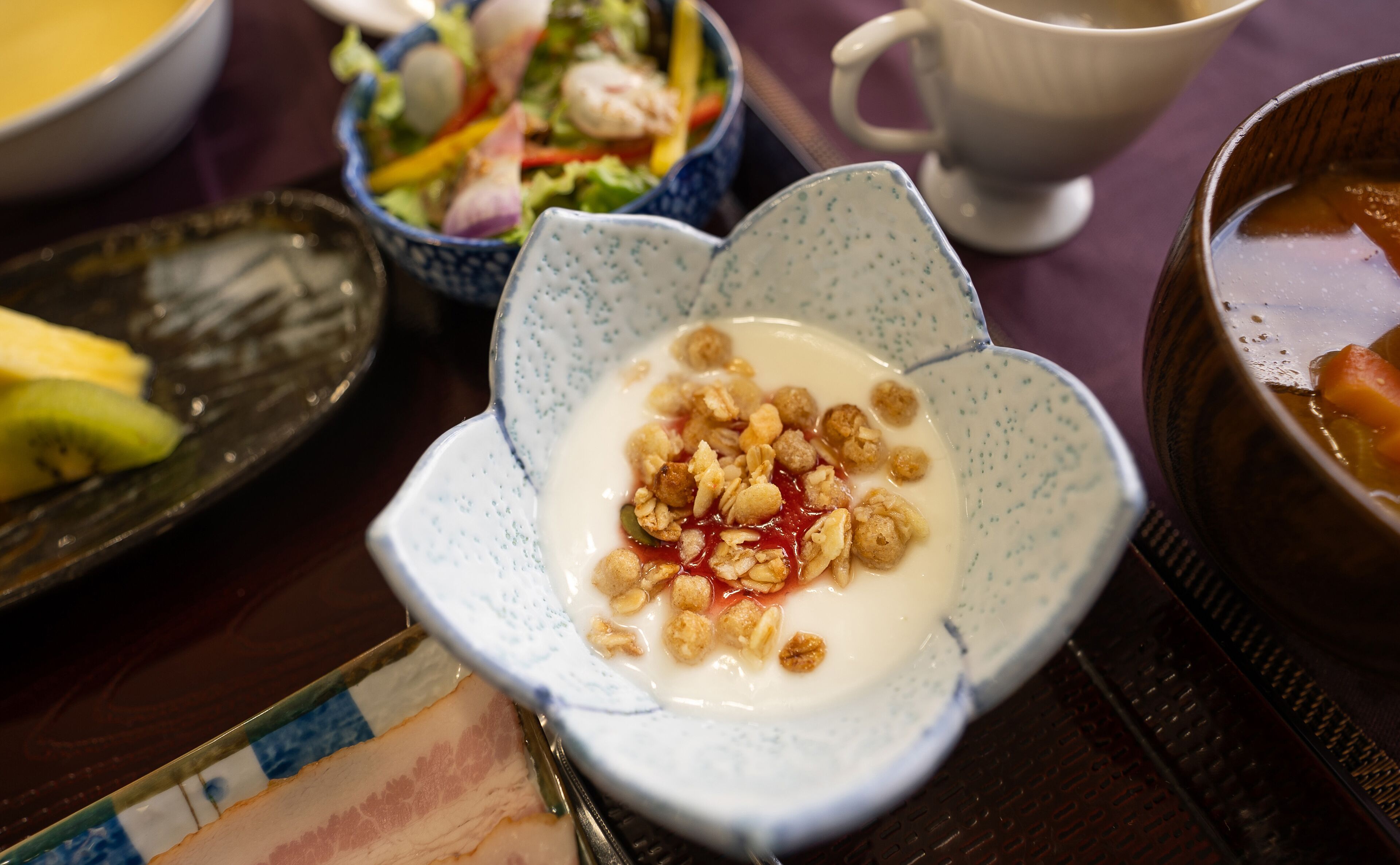 A table with various dishes including a bowl of yogurt with granola and fruit, a salad, and a bowl of soup.