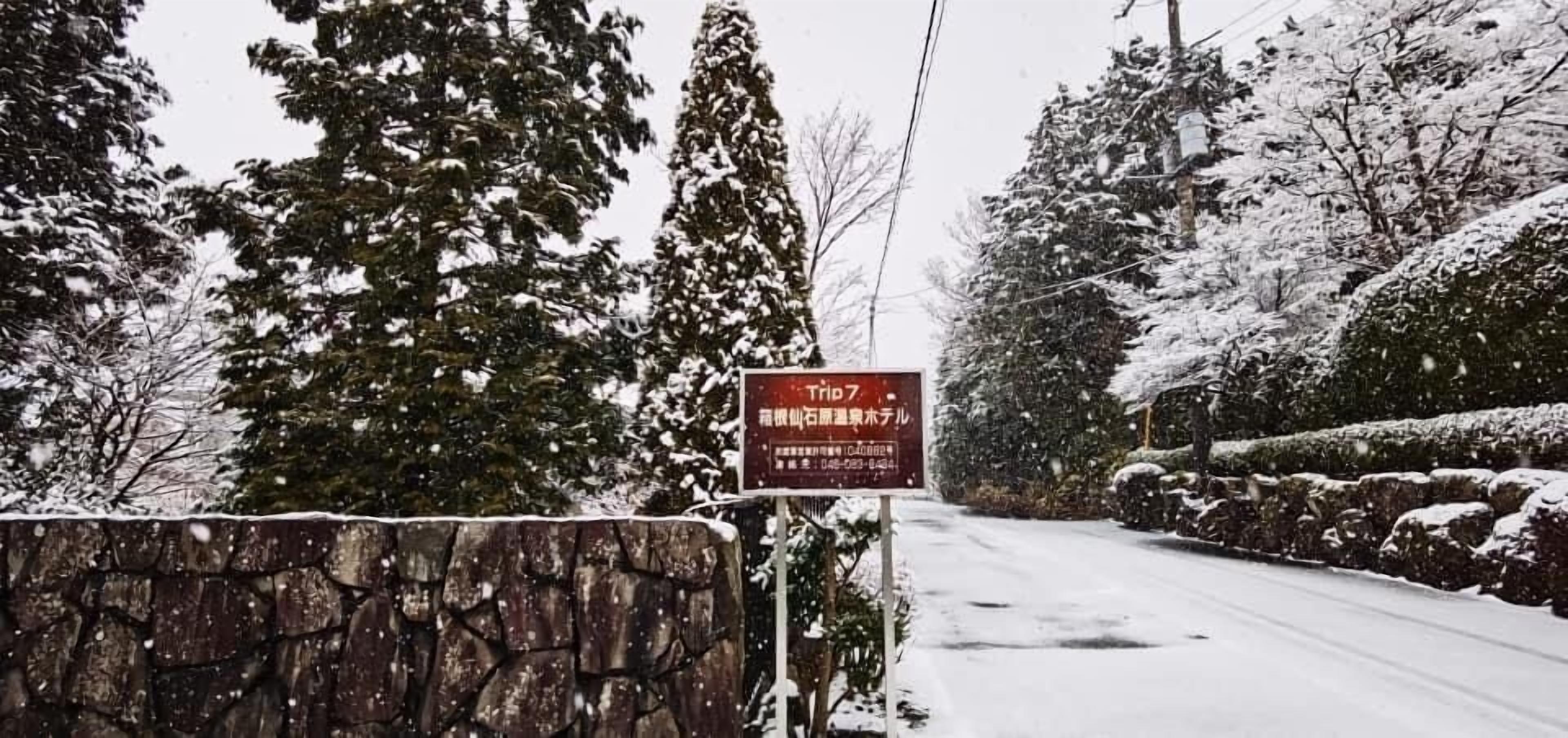 Et skilt med japansk tekst på en stenvæg ved siden af en sneklædt vej.