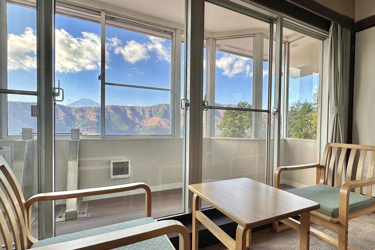 Un balcon avec une table et deux chaises, une vue sur les montagnes et une fenêtre donnant sur le ciel.