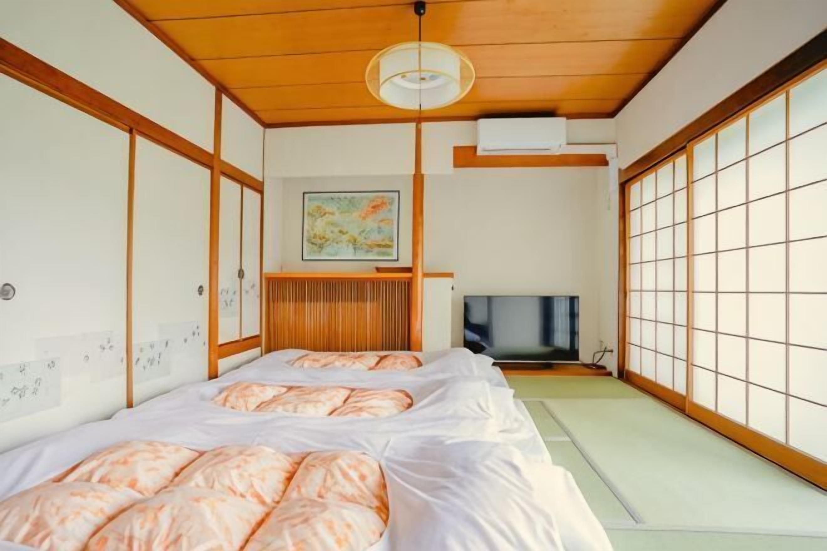 A traditional Japanese-style room with tatami flooring, two beds with pink bedding, a television, and a sliding door.