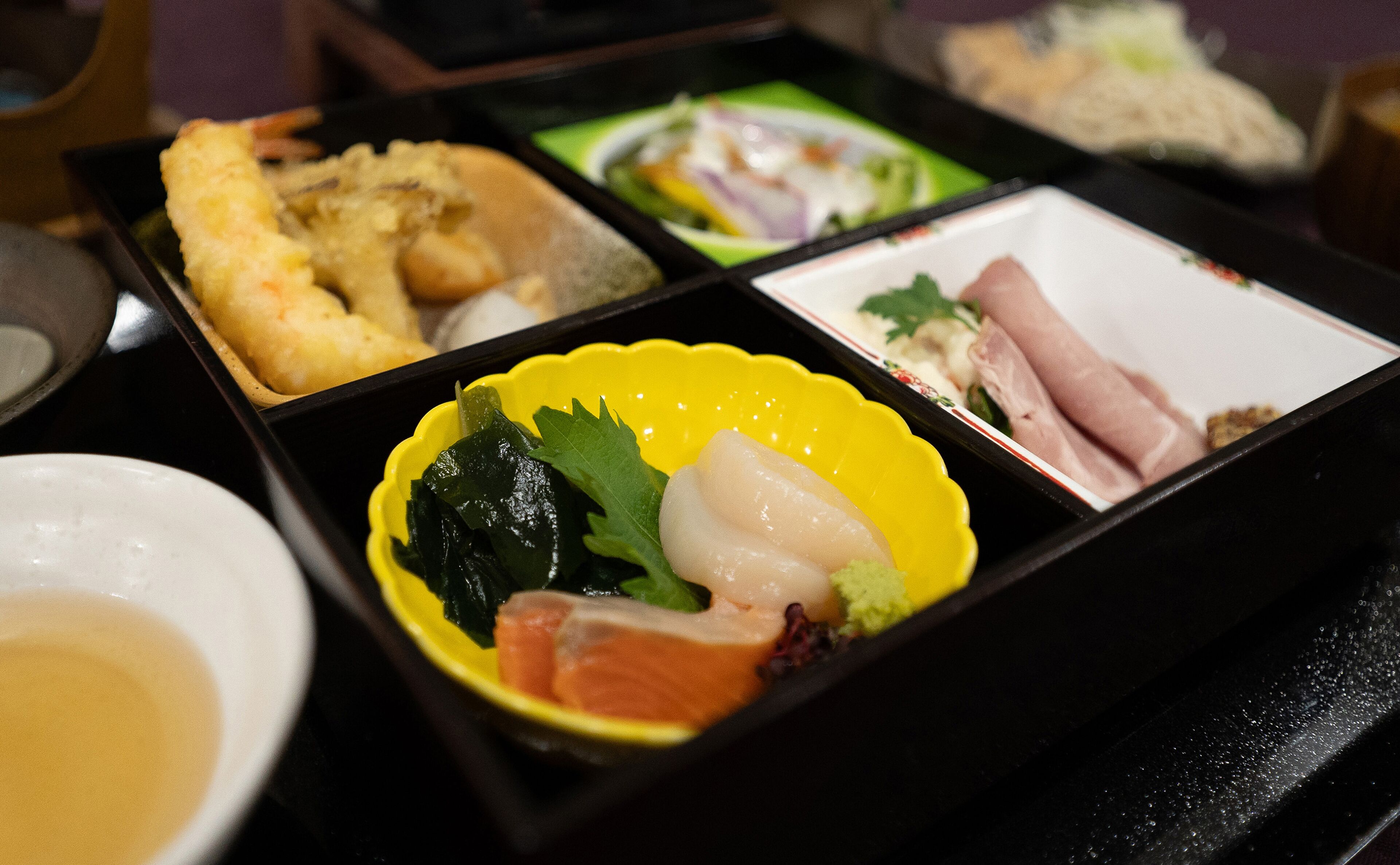 A bento box with various food items including fish, vegetables, and rice.