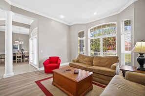 A spacious living room with a large window, a red armchair, a beige sofa, and a wooden coffee table. - Private Pool Home on the East End of PCB – Minutes to the Beach (Panama City)