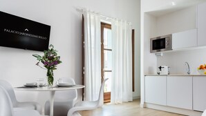 A modern, minimalist living space with a dining area, kitchen, and a flat-screen TV displaying "PALACIO JARDINESBMURILLO". - PALACIO BUENAVISTA LUXURY APARTMENTS 1.1. (Sevilla)
