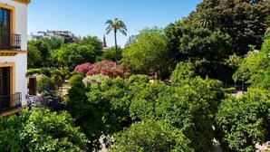 A lush garden with various trees and shrubs, a palm tree, and a building with balconies. - PALACIO BUENAVISTA LUXURY APARTMENTS 1.1. (Sevilla)