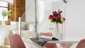 A modern dining area with a glass partition, a white table, pink chairs, and a vase with flowers. - PALACIO BUENAVISTA LUXURY APARTMENTS B.2 (Sevilla)
