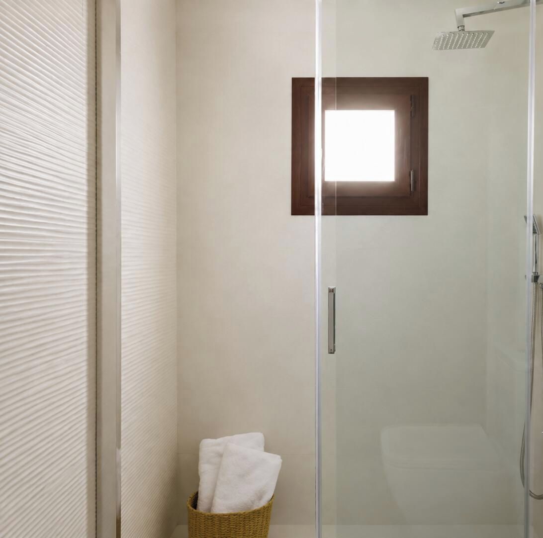 A glass-enclosed shower area with a wooden door frame and a towel basket.