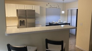 A kitchen with white cabinets, a stainless steel refrigerator, a bar counter, and two chairs. - Private Paradise! Beautiful Villa with game room  and private pool great getaway (Haines City)