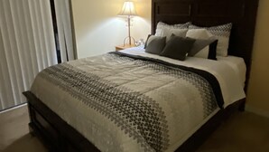 A neatly made bed with a patterned bedspread, a bedside lamp, and a painting on the wall. - Private Paradise! Beautiful Villa with game room  and private pool great getaway (Haines City)