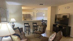A living room with a sofa, armchair, TV, and a dining area with chairs and a kitchen in the background. - Private Paradise! Beautiful Villa with game room  and private pool great getaway (Haines City)