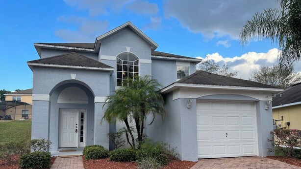 A two-story house with a garage, a front entrance with a door, and a small garden with a palm tree. - Private Paradise! Beautiful Villa with game room  and private pool great getaway (Haines City)