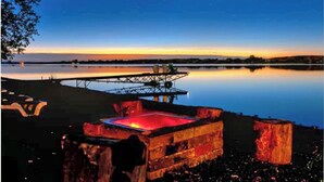 Un lac paisible au crépuscule, avec un quai et une structure en bois illuminée d’une lumière rouge.