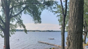 Un cadre idyllique au bord du lac, avec des canoës alignés contre un arbre, une jetée s’avançant dans l’eau et une vue dégagée sur le lac.