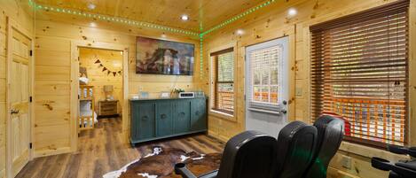 Interior de una cabaña de madera con comedor, cocina y un ventanal con persianas.