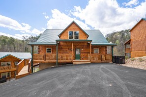 A log cabin with a green metal roof, a front porch, and a driveway leading to the entrance.
