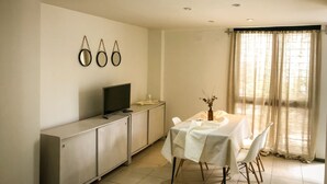 Zona pranzo con tavolo apparecchiato per quattro persone, televisore su un mobile e tre specchi a parete.