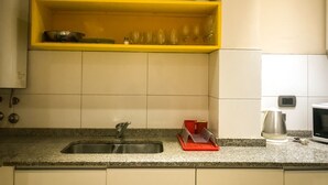Una cucina con un piano di lavoro in granito, un lavello in acciaio inossidabile, uno scaffale giallo sopra il lavello e un forno a microonde a destra.