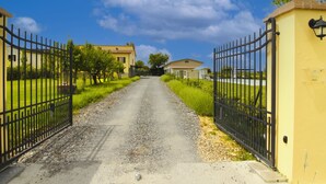 Un camino de grava que conduce a una entrada con puerta, con un edificio amarillo a la derecha y uno blanco a la izquierda.