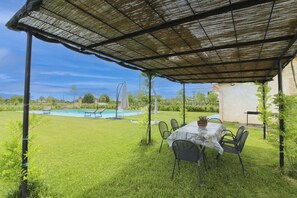 Un espace extérieur abrité comprenant une piscine, une table avec des chaises et une pelouse.