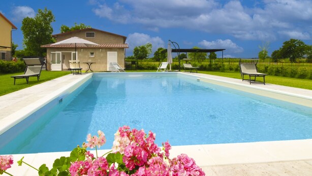 Una piscina rectangular con sillones de descanso y una pérgola en un día soleado.