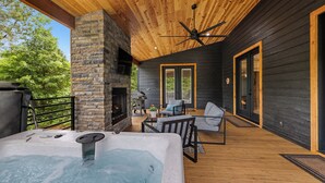 Eine Holzterrasse mit Kamin aus Stein, Sitzgelegenheiten im Freien und einem Whirlpool.