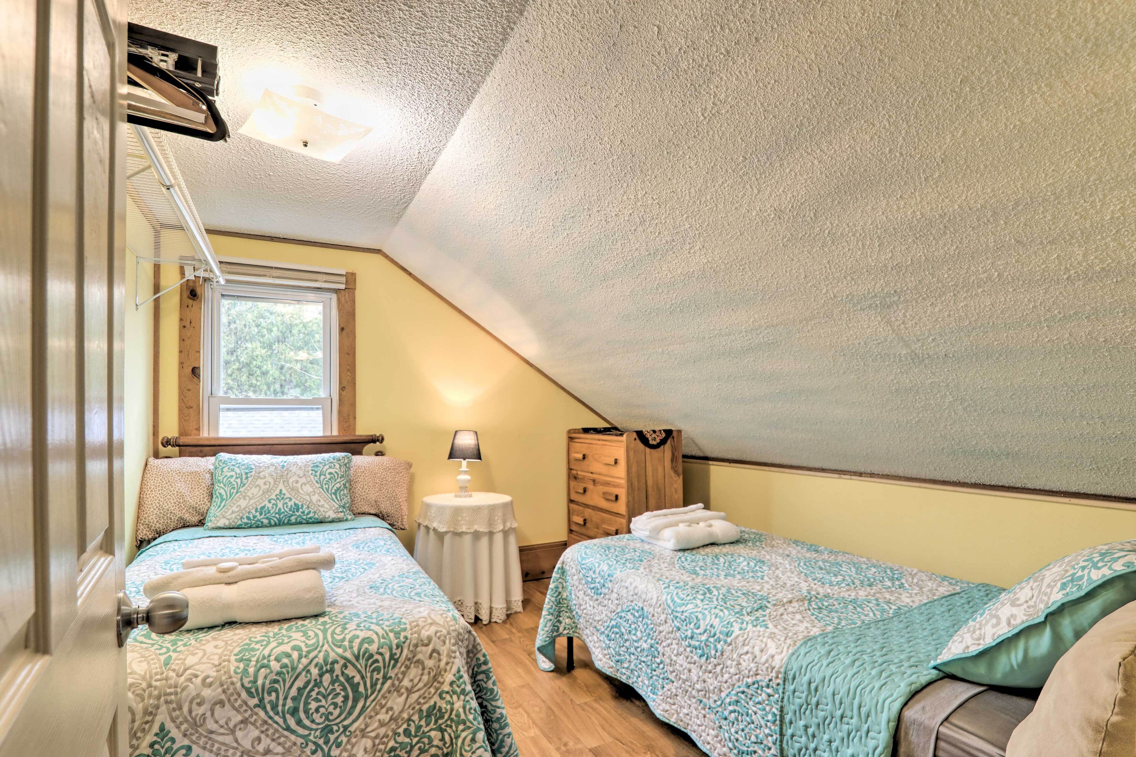 A bedroom with two beds, a window, a lamp, and a dresser.