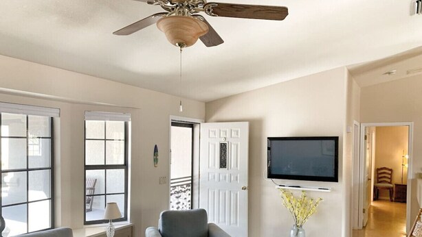 Un vaste salon doté d’un ventilateur de plafond, d’un téléviseur à écran plat fixé au mur et d’une grande fenêtre laissant entrer la lumière naturelle.