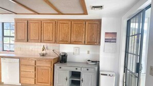 Une cuisine avec des meubles de rangement en bois, un lave-vaisselle blanc, un plan de travail gris et un petit évier.