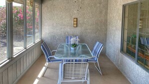 Une véranda avec une table et des chaises, un ventilateur de plafond et une horloge au mur.