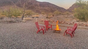 Une terrasse en gravier avec quatre chaises Adirondack rouges et un petit foyer.